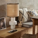 Lampe à poser Venus en céramique blanche avec abat-jour en fibre naturelle sur une table, décorée de coussins et d'objets décoratifs.