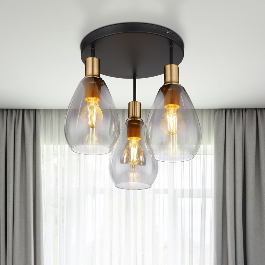 Plafonnier Fanni 3 lampes allumées, créant une ambiance chaleureuse avec son design en métal laiton et verre fumé – Dakar, Sénégal.